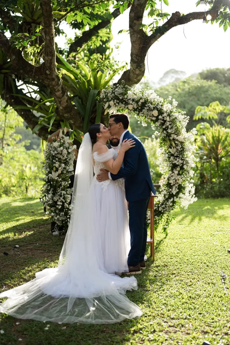 Casamento ao ar livre — beijo dos noivos sob arco de flores
